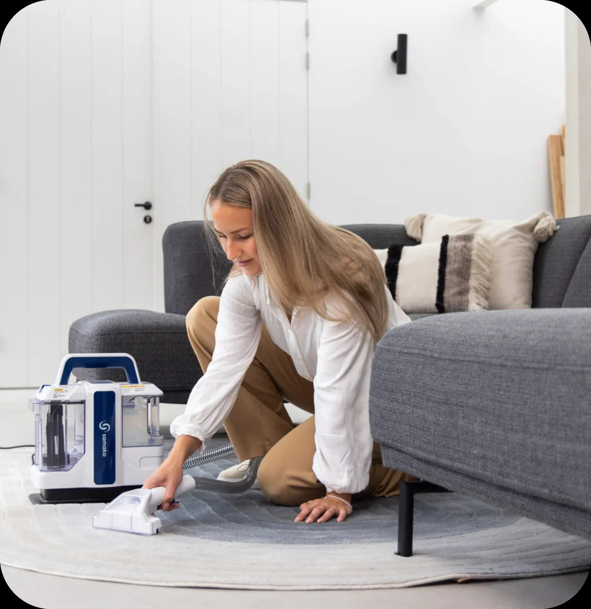 Woman cleaning a rug with the Samako PowerClean Pro beside a grey sofa